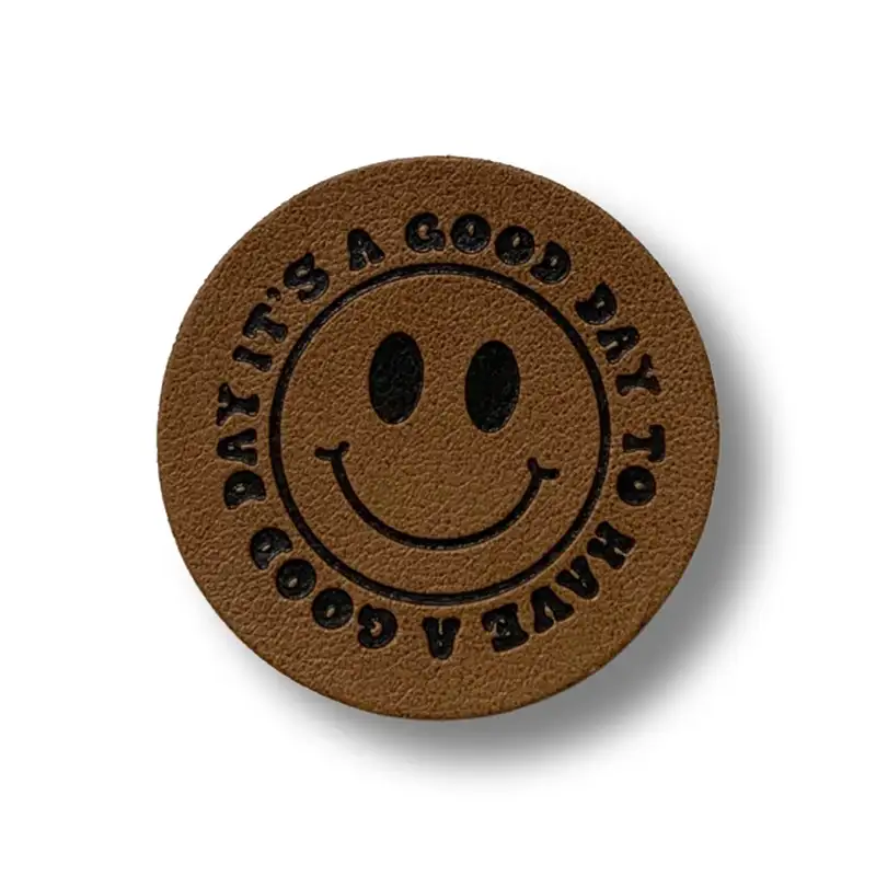 runder Aufnäher aus Kunstleder mit Smiley Motiv und rundem Schriftzug It's a good day to have a good day"