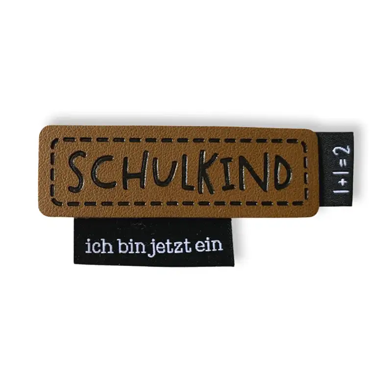 Lederlabel mit Aufdruck Schulkind. Schwarzes Weblabel mit Aufdruck ich bin jetzt ein. Schwarzes Weblabel mit Aufdruck 1 + 1 =2